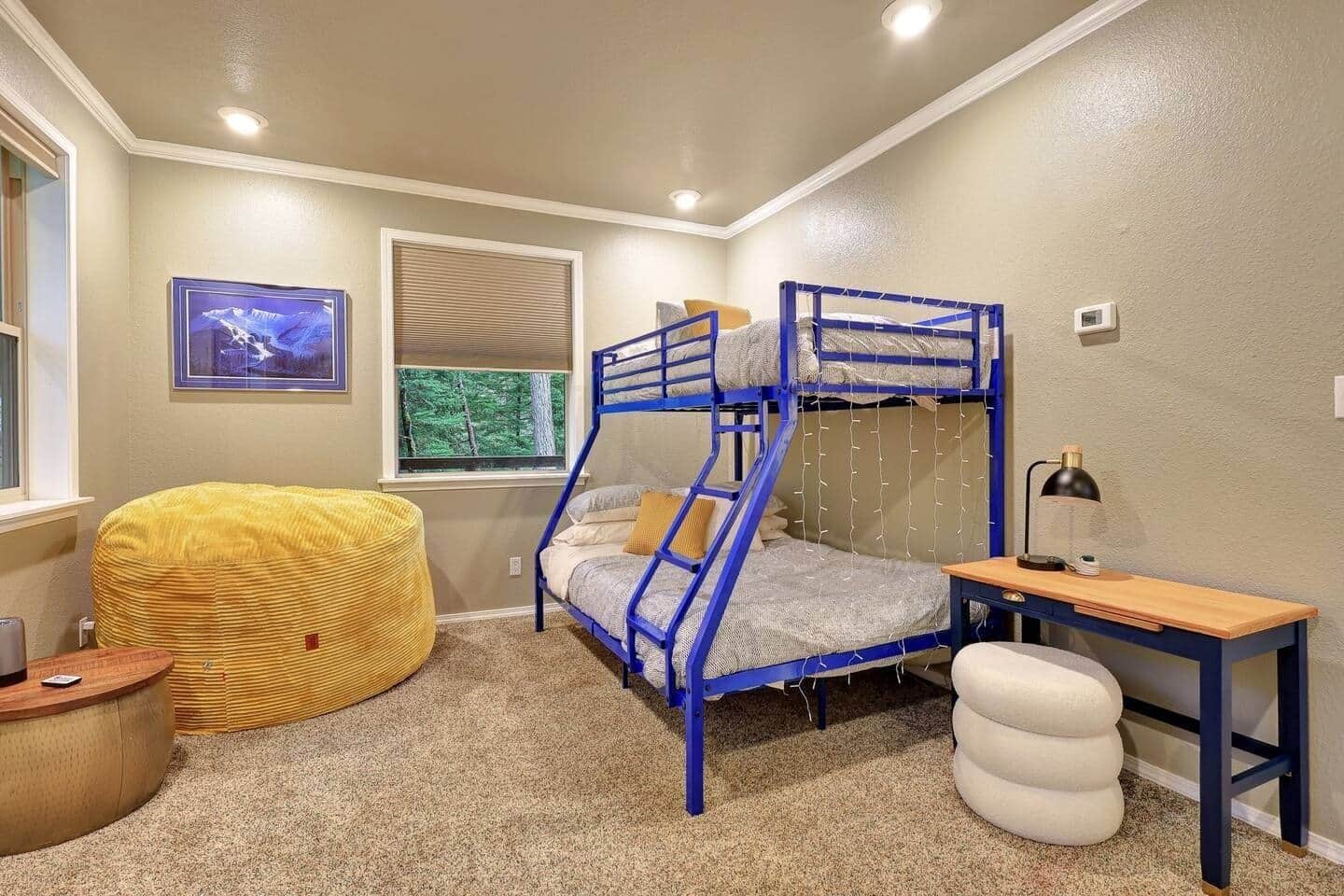 A bunk bed with a desk and chair, a yellow bean bag, and a window with blinds.