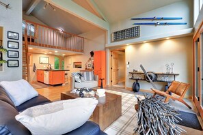 A spacious living area with a sofa, coffee table, and a chair. A kitchen is visible in the background, and there is a balcony with a railing.
