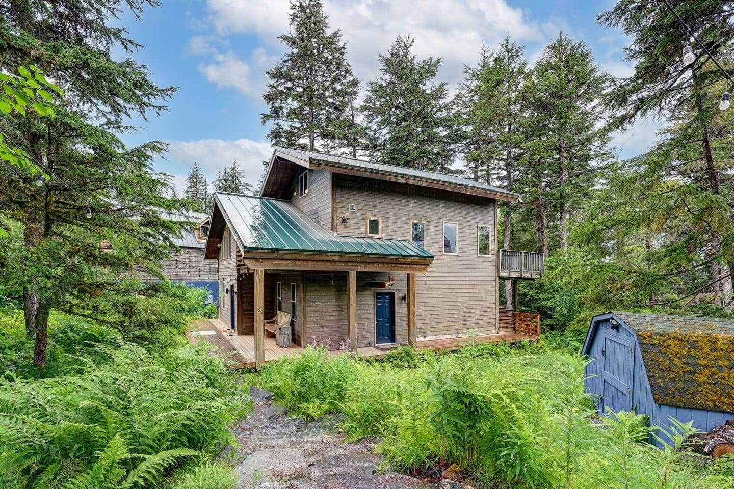 A two-story wooden cabin with a porch, surrounded by dense forest.
