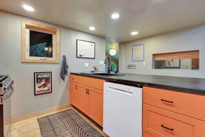 Una cocina con armarios color naranja, lavavajillas, estufa y ventana con vista a árboles.