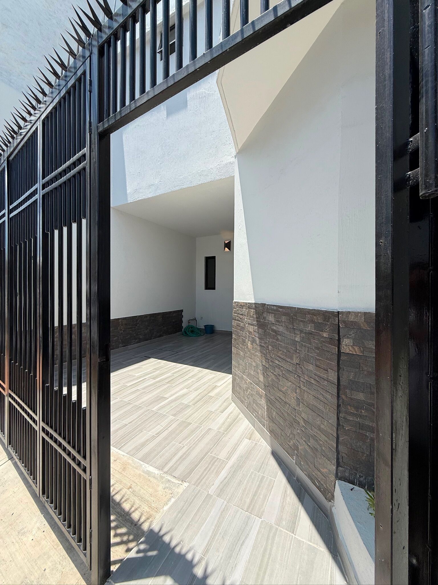 A gated entrance to a building with a tiled patio area and a stone wall.