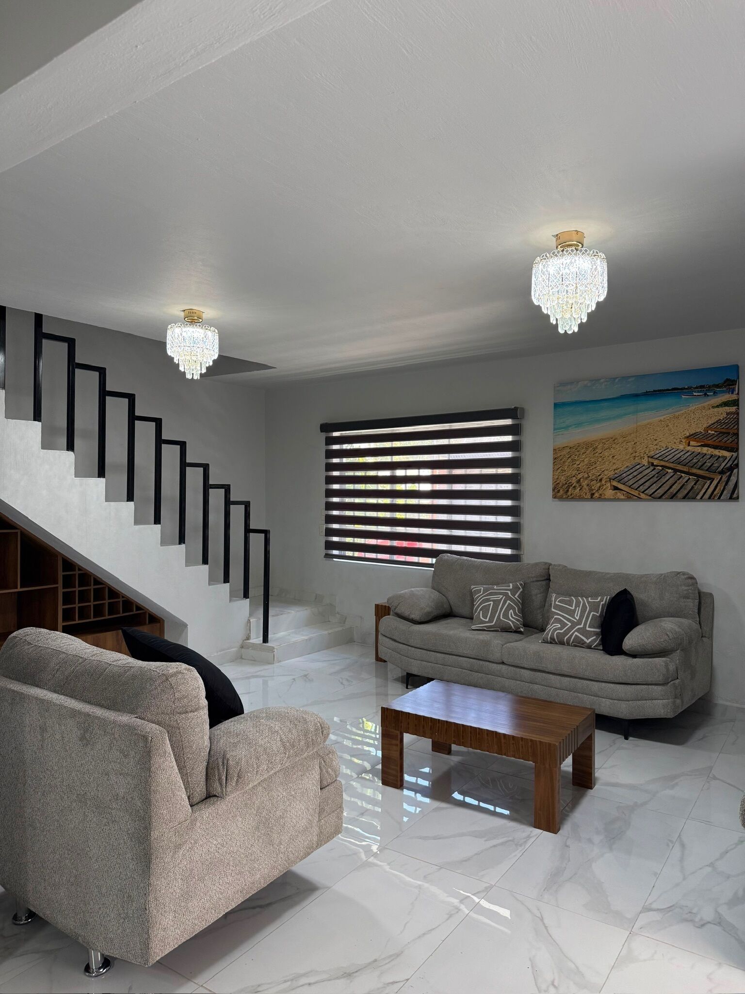 Una sala de estar moderna con una escalera, un sofá, una mesa de centro y un cuadro de una playa.