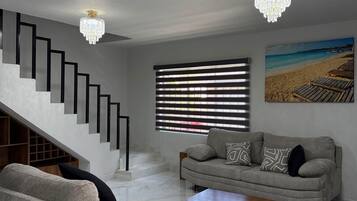 Una sala de estar moderna con una escalera, un sofá, una mesa de centro y un cuadro de una playa.