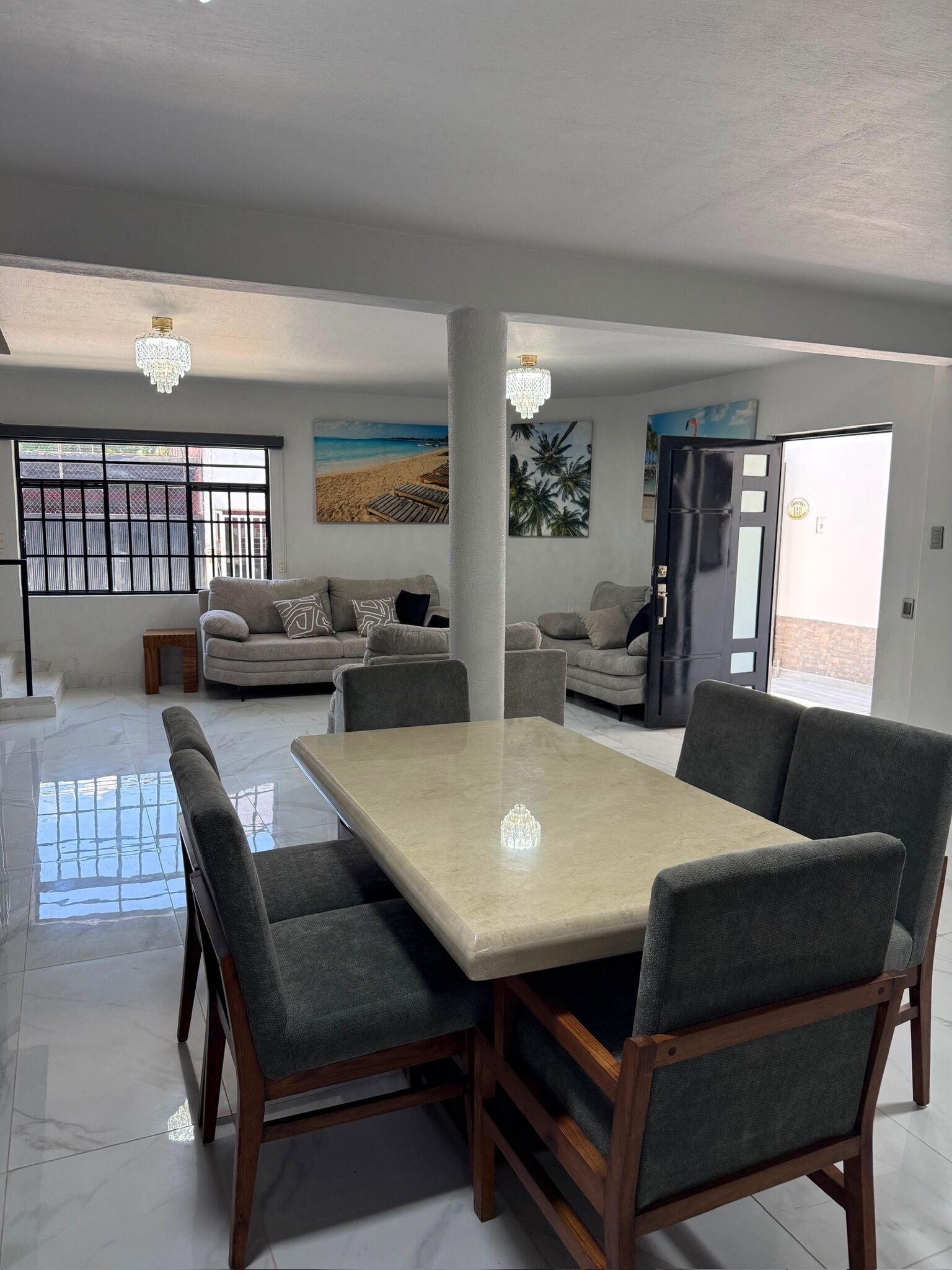 A spacious living area with a large dining table, multiple sofas, and a view of the outdoors through a large window.