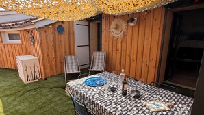 Un área de comedor al aire libre con una mesa preparada para dos personas, rodeada de paredes de madera y un paraguas decorativo.