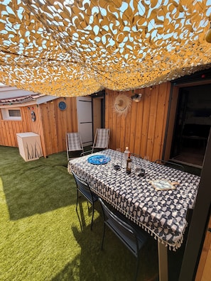 An outdoor dining area with a table set for two, surrounded by wooden walls and a decorative umbrella. - Ferdinand's Cabin • Beach: 2 min • Private patio • Air Conditioning • Fiber (Arcachon)