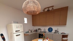 Una cocina moderna con un refrigerador blanco, armarios de madera, una mesa redonda con sillas y una lámpara colgante.