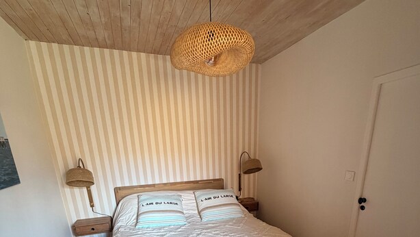 Un dormitorio con cama de madera, papel tapiz a rayas y una lámpara de techo de fibras naturales.