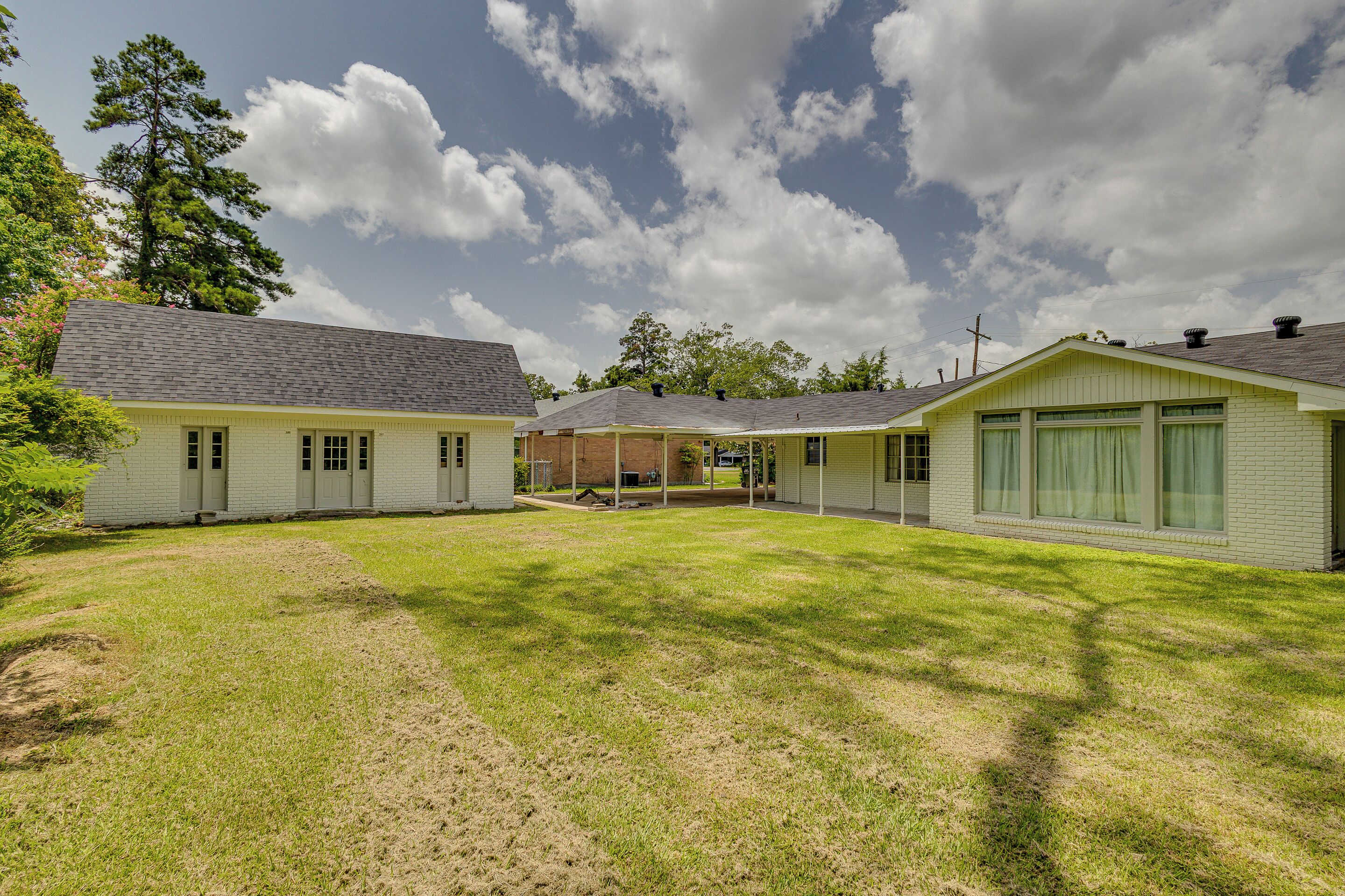 A residential property with a grassy yard, a brick house, and a covered porch.
