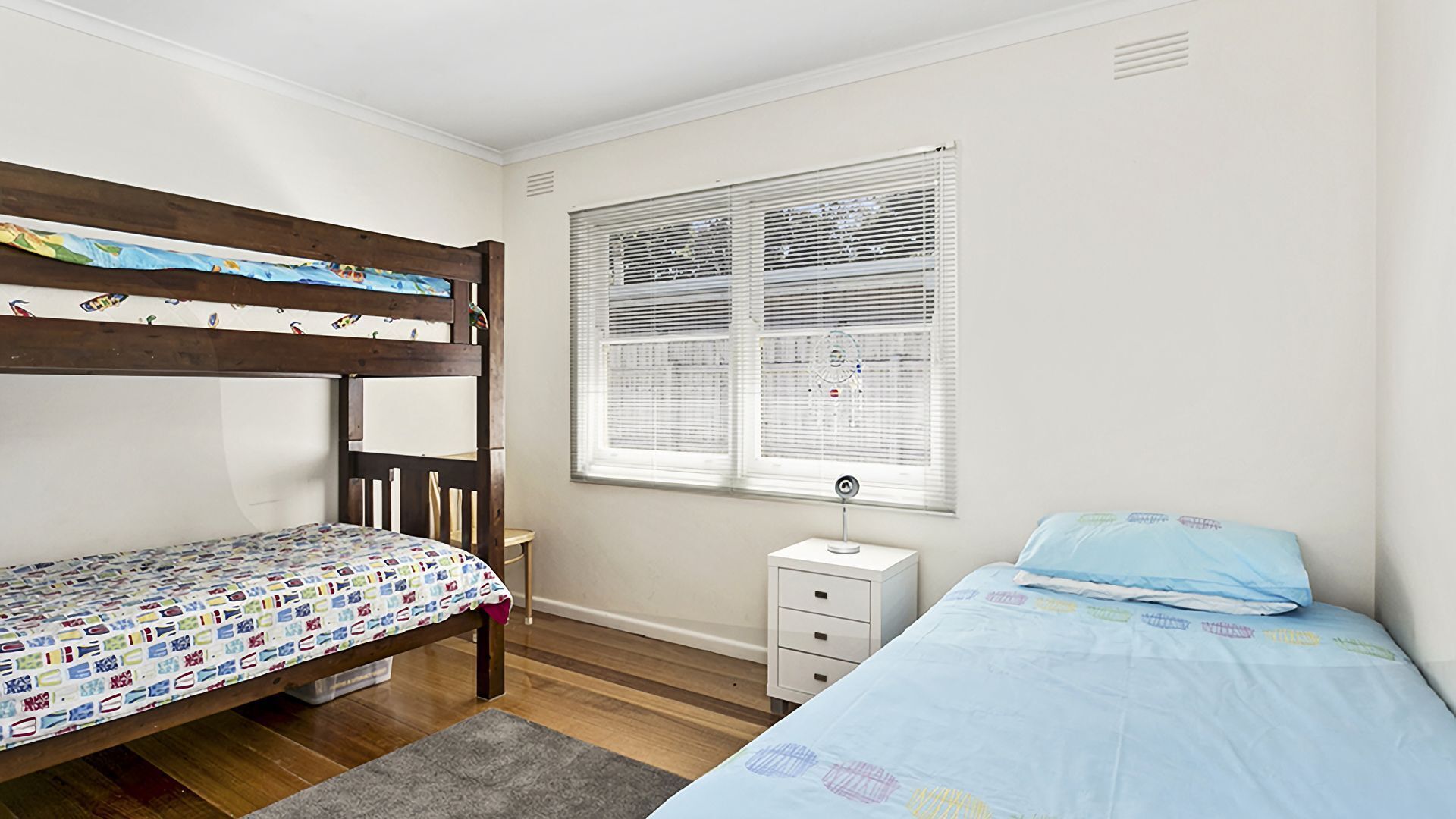 Een slaapkamer met een stapelbed, een enkel bed, een nachtkastje en een raam met zonwering.