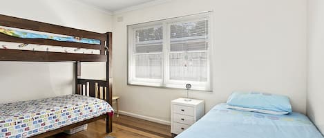 A bedroom with a bunk bed, a single bed, a bedside table, and a window with blinds.