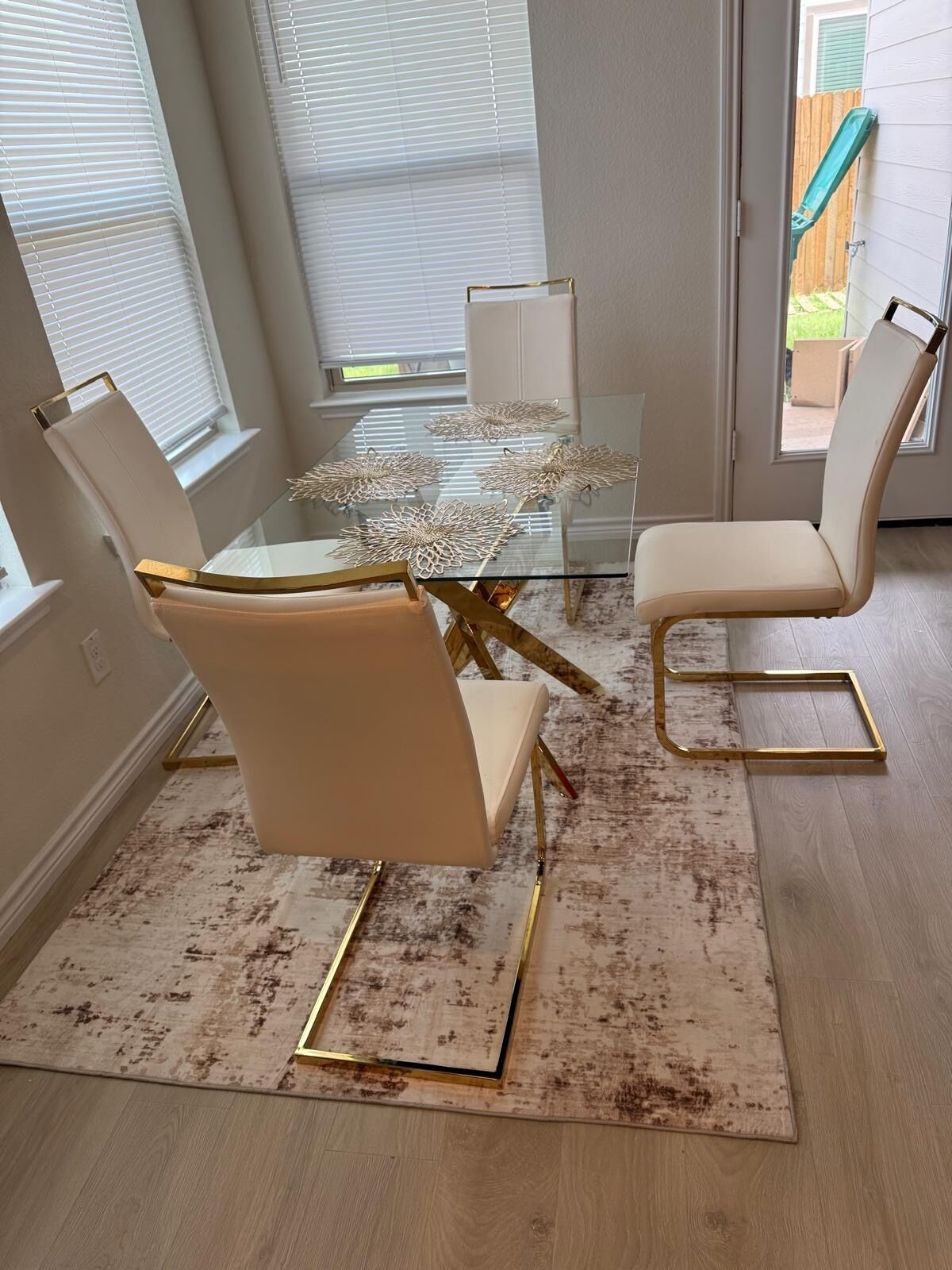 A dining area with a glass table surrounded by chairs, a patterned rug, and a view of the outside.