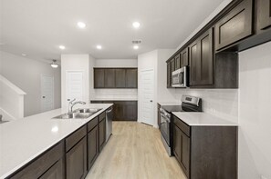 A modern kitchen with dark cabinets, white countertops, and a central island. - Luxurious 6-bedroom house near UNT & Medical City (Denton)