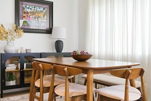A dining area with a wooden table and chairs, a bowl of salad, a lamp, and a framed picture on the wall.