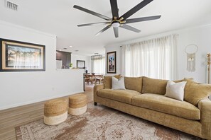 A modern living room with a sofa, a ceiling fan, and a dining area in the background.