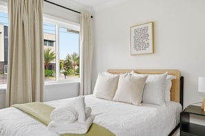 A hotel room with a bed, a window with curtains, a wall-mounted picture, and a bedside table with a lamp.