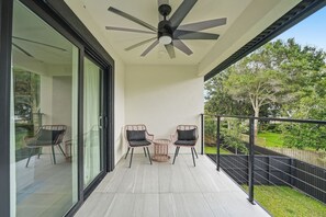 Ein Balkon mit Deckenventilator, zwei Korbstühle, einem kleinen Tisch und einer Glastür, die zu einem Zimmer führt.