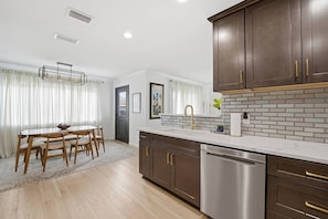 A modern kitchen with a white countertop, stainless steel appliances, and dark wooden cabinets. - Anastasia Island Retreat - Villa B - Walk Downtown (St. Augustine)