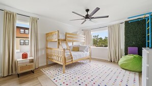 Un dormitorio con una cama litera, un ventilador de techo, una ventana con cortinas, un sillón de cuero verde y un tapete de lunares.