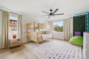A bedroom with a bunk bed, a ceiling fan, a window with curtains, a green bean bag, and a polka dot rug. - Anastasia Island Retreat - Villa B - Walk Downtown (St. Augustine)