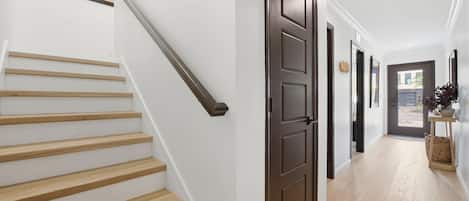 Una escalera con escalones de madera y una barandilla oscura, que conduce a una puerta con marco oscuro.