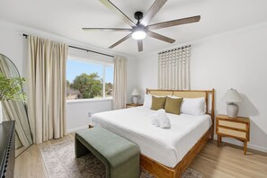 Ein Hotelzimmer mit einem Bett, Nachttischen, einem Deckenventilator, einem Fenster mit Vorhängen und Blick nach außen.