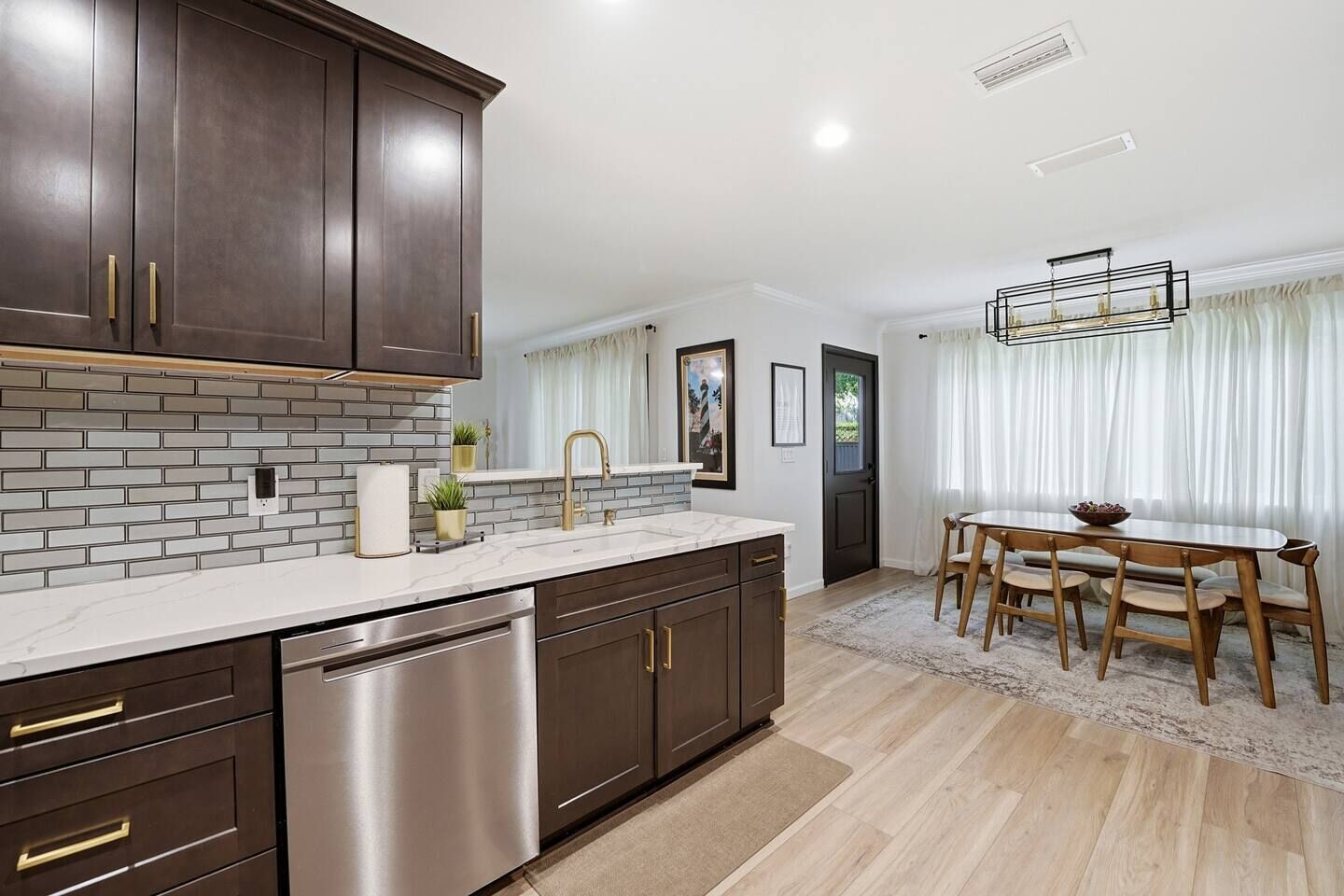 A modern kitchen with dark cabinetry, a stainless steel dishwasher, and a marble countertop.