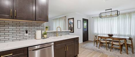 A modern kitchen with dark cabinetry, a stainless steel dishwasher, and a marble countertop.
