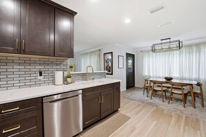 A modern kitchen with dark cabinetry, a stainless steel dishwasher, and a marble countertop.