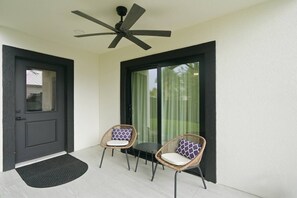 A balcony with two wicker chairs, a ceiling fan, and a door with a black mat. - Anastasia Island Retreat - Villa A - Walk Downtown (St. Augustine)