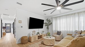 A modern living room with a flat-screen TV, a ceiling fan, a sofa set, and a coffee table.