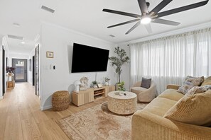 Ein modernes Wohnzimmer mit Flachbildfernseher, Deckenventilator, Sofagarnitur und Couchtisch.