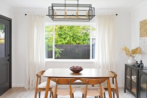 A dining area with a table and chairs, a window with curtains, and a cabinet with a vase. - Anastasia Island Retreat - Villa A - Walk Downtown (St. Augustine)