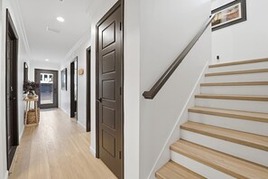 A hallway with a wooden floor, a dark brown door, and a staircase with wooden steps and a metal handrail.