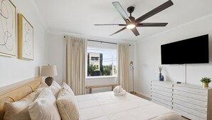A hotel room with a bed, a desk, a television, and a ceiling fan.