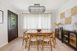 Ein Essbereich mit einem Holztisch und Stühlen, einer Kristallleuchtre, einem Fenster mit Vorhängen und einem Wanddekor.