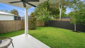 A backyard with a patio, a ceiling fan, a wooden fence, and a tree.