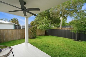 Ein Garten mit Terrasse, Deckenventilator, Holzzaun und Baum.