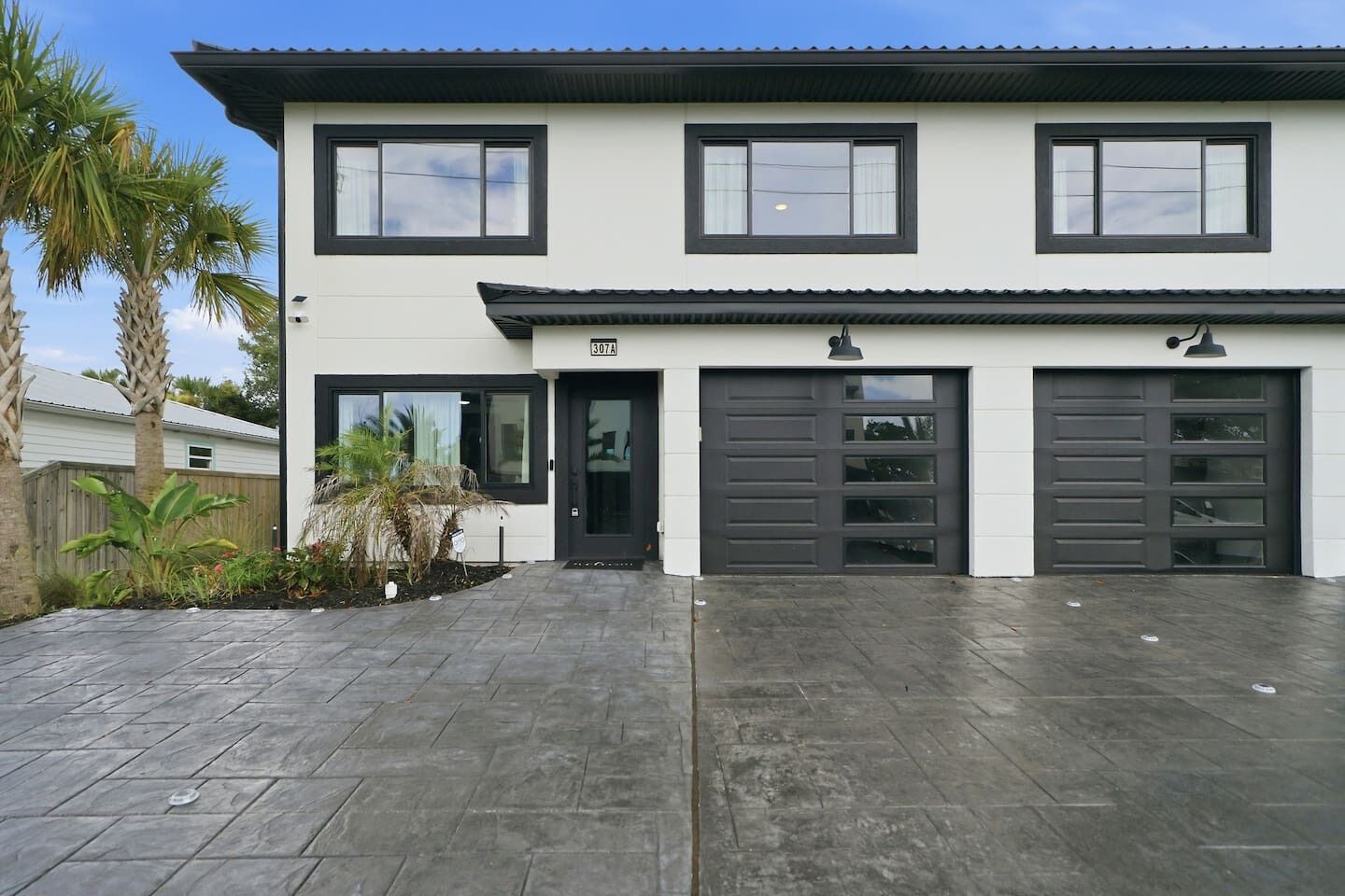 Une maison moderne à deux étages, dotée d’un garage, d’une allée et d’un jardin bien entretenu.