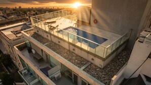 En pool på taket med glasräcken, en sittgrupp och utsikt över stadsbilden.