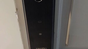 En svart elektronisk apparat med en rund knapp, en liten display och varumärket ”TENON” på undersidan.