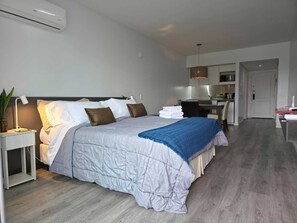 A modern hotel room with a bed, bedside table, lamp, and a view into the kitchen area. - Skyline Studio - Panoramic View - Open 24 hours a day. Gym, Sauna, Laundry. Views. (Buenos Aires)