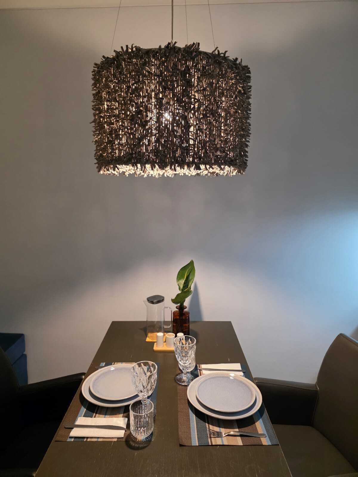 A dining area with a table set for two, a hanging light fixture, and a potted plant.