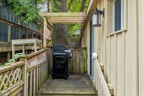 Ein schmaler Holzweg führt zu einem Grill, umgeben von Holzzäunen und einem Baum.