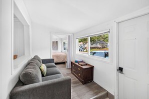 Ein schmaler Flur mit einem grauen Sofa, einer Holzkommode und einem Bett im Hintergrund.