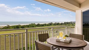 A balcony with a table and chairs, overlooking a beach and ocean. - Coastal SurfWatch Getaway with Ocean Vista & Spacious 2BR Comfort (Hilton Head Island)