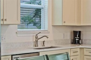 Una cocina con ventana, un lavamanos y una cafetera.