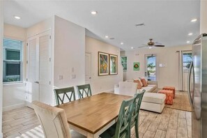 A modern dining area with a wooden table and chairs, a white sofa, and a ceiling fan. - Margaritaville 4BR | Sleeps 10 | Near Disney (Kissimmee)