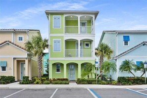 A multi-story residential building with a green facade, balconies, and a parking lot in front. - Margaritaville 4BR | Sleeps 10 | Near Disney (Kissimmee)