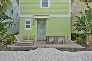 Ein zweistöckiges Gebäude mit grüner Fassade, einer Haustür und einem Patio mit Gartenmöbeln.